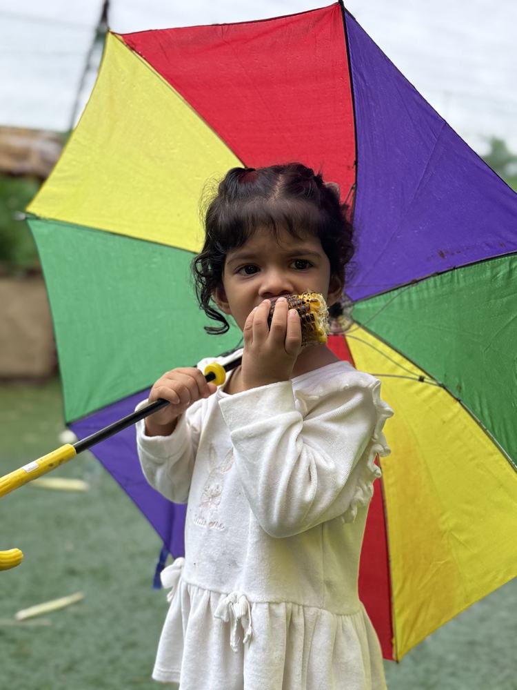 A little girl eating roasted corn under a rainbow umbrella